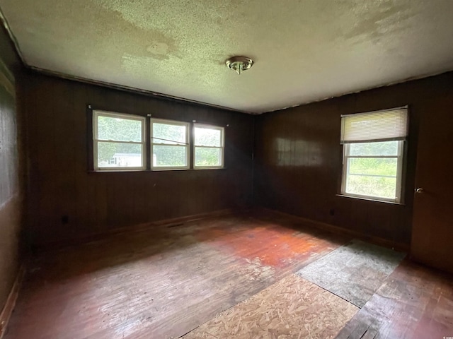 empty room with a textured ceiling, light hardwood / wood-style flooring, and wood walls