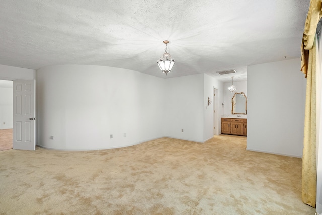 spare room featuring a textured ceiling, an inviting chandelier, and light carpet