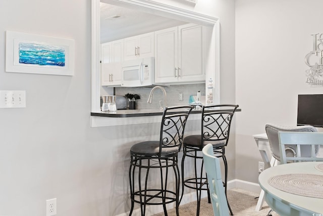 kitchen with sink, white cabinetry, decorative backsplash, and a breakfast bar area