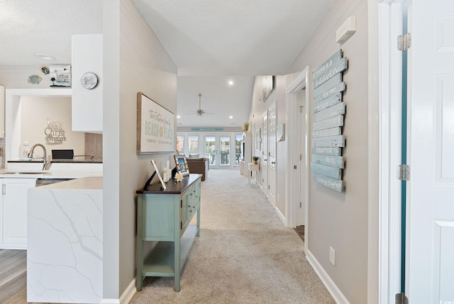 hallway with light carpet, a textured ceiling, sink, and french doors