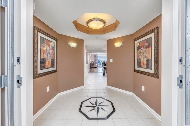 hallway featuring a tray ceiling and light tile patterned floors