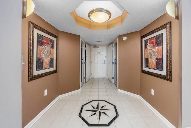 hallway featuring a textured ceiling, a tray ceiling, and light tile patterned floors