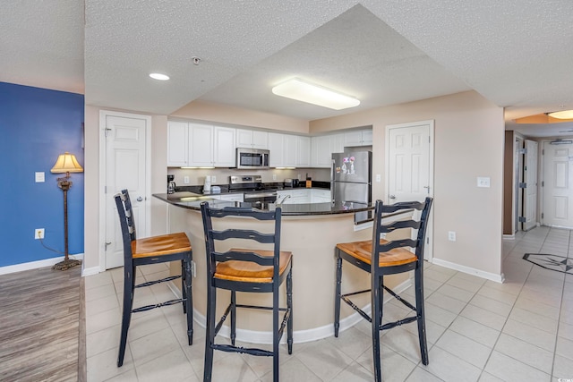 kitchen with white cabinets, kitchen peninsula, a textured ceiling, stainless steel appliances, and a kitchen breakfast bar