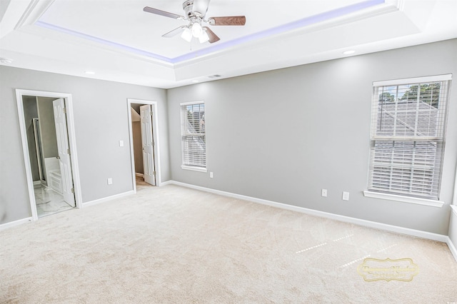 unfurnished bedroom featuring a raised ceiling, connected bathroom, ceiling fan, and a walk in closet