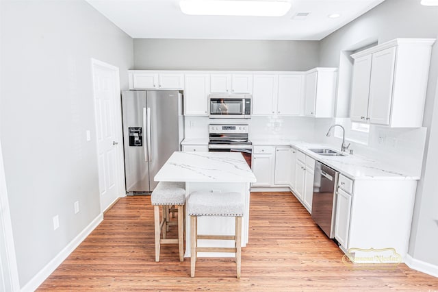 kitchen featuring white cabinets, sink, appliances with stainless steel finishes, a center island, and light hardwood / wood-style floors