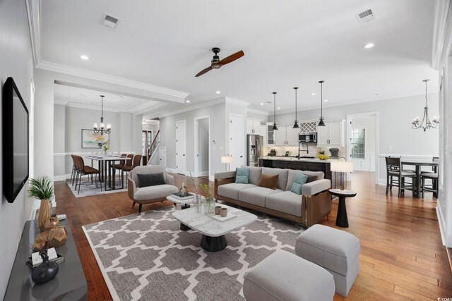 living room featuring ceiling fan with notable chandelier, crown molding, hardwood / wood-style floors, and sink