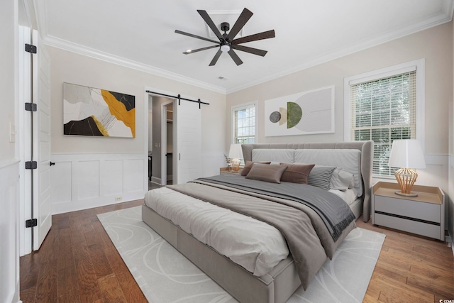 bedroom with a barn door, wood-type flooring, crown molding, and ceiling fan