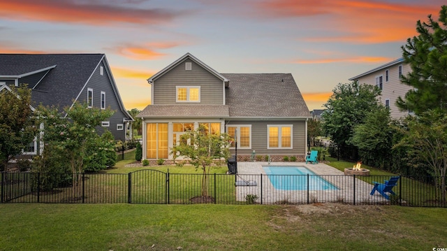 back house at dusk with a lawn and a fenced in pool