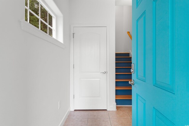 foyer entrance featuring light tile patterned flooring, baseboards, and stairway