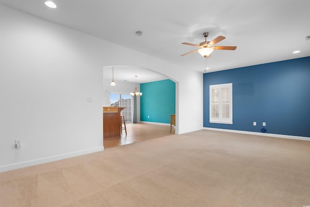 empty room featuring light carpet, baseboards, ceiling fan with notable chandelier, arched walkways, and recessed lighting