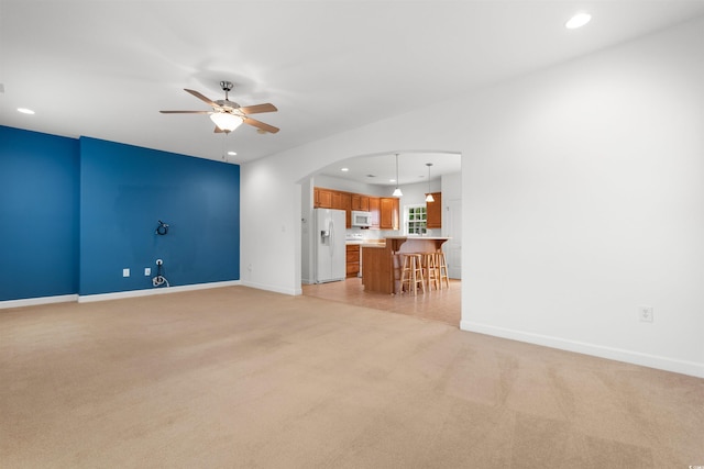unfurnished living room featuring a ceiling fan, light carpet, arched walkways, and recessed lighting
