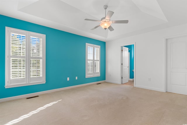 unfurnished bedroom featuring carpet flooring, a raised ceiling, baseboards, visible vents, and ceiling fan