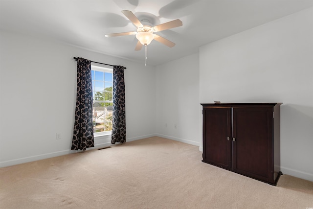 spare room with light colored carpet, visible vents, baseboards, and a ceiling fan