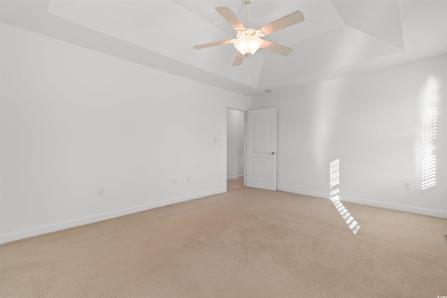 spare room featuring light carpet, baseboards, a ceiling fan, and a raised ceiling