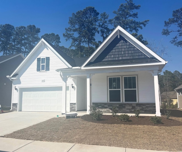 view of front of house with driveway, stone siding, a garage, and a porch