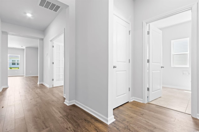 hall featuring baseboards, visible vents, and wood finished floors