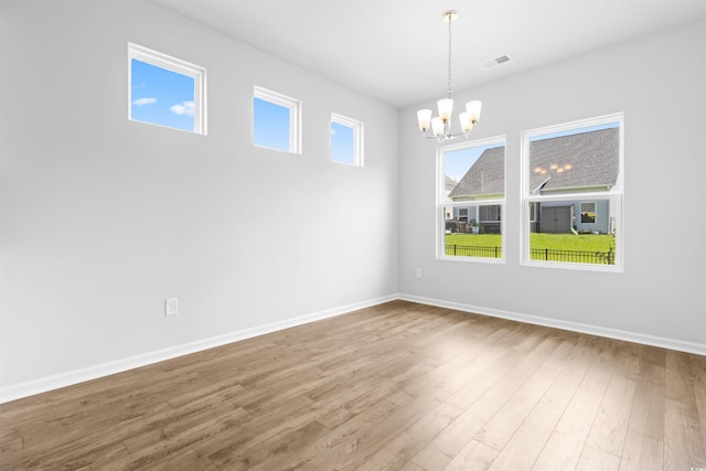 empty room with a chandelier, visible vents, baseboards, and wood finished floors