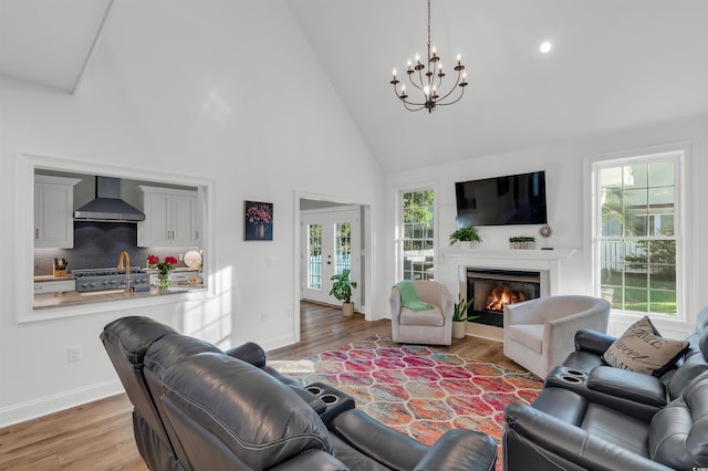 living room featuring an inviting chandelier, a glass covered fireplace, wood finished floors, high vaulted ceiling, and baseboards