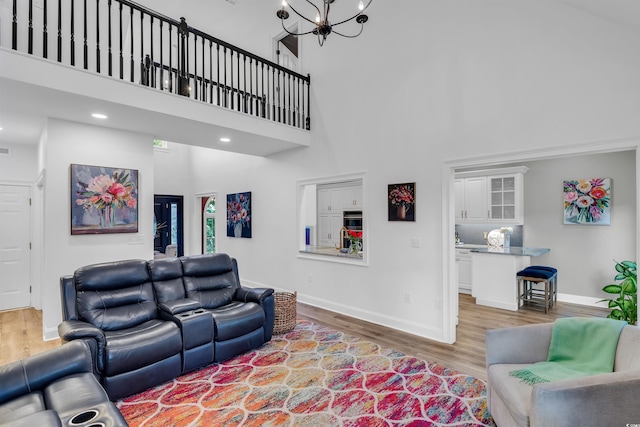 living area featuring a notable chandelier, recessed lighting, a towering ceiling, light wood-type flooring, and baseboards