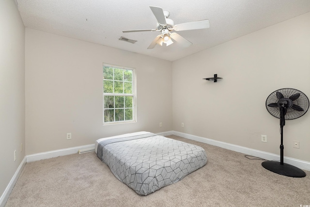 bedroom with a textured ceiling, light colored carpet, and ceiling fan