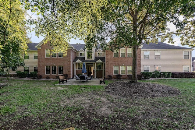 rear view of property featuring brick siding, a patio, and a lawn