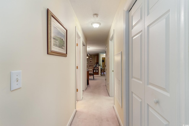 hall with a textured ceiling, light colored carpet, and baseboards