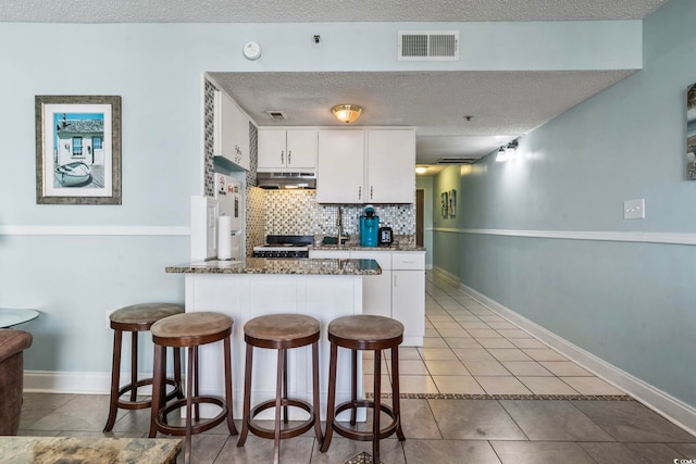 kitchen with a textured ceiling, decorative backsplash, dark stone counters, and white cabinets