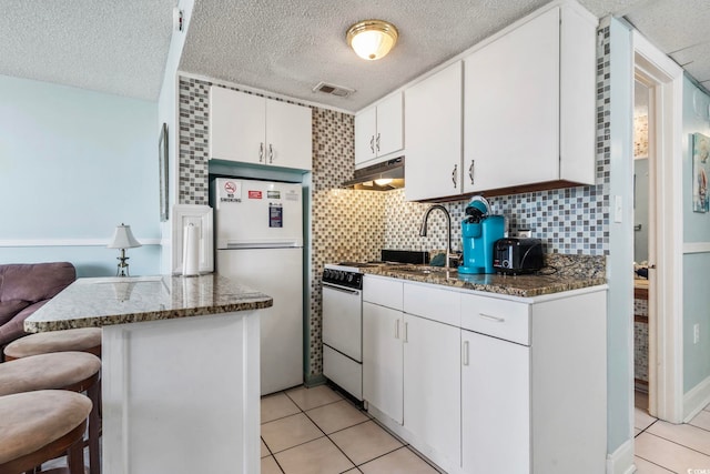 kitchen featuring a kitchen bar, refrigerator, dark stone countertops, and white cabinets