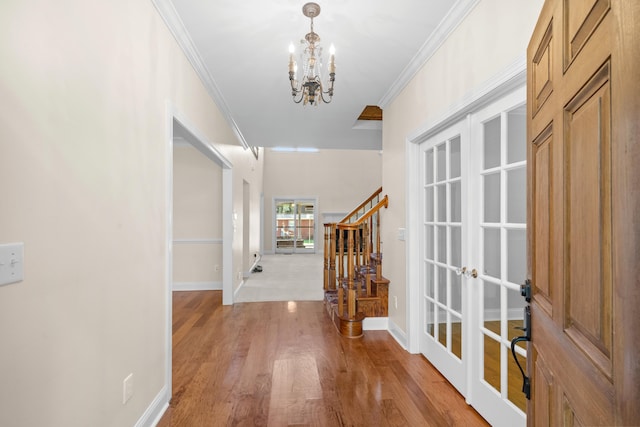 foyer featuring light hardwood / wood-style flooring, ornamental molding, a notable chandelier, and french doors