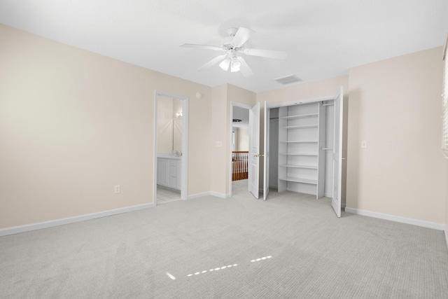 unfurnished bedroom featuring light carpet, a closet, ensuite bath, and ceiling fan