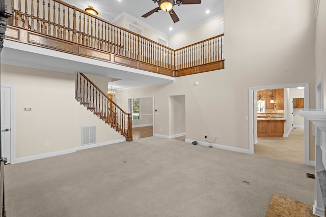 unfurnished living room with a high ceiling, crown molding, ceiling fan with notable chandelier, and light colored carpet