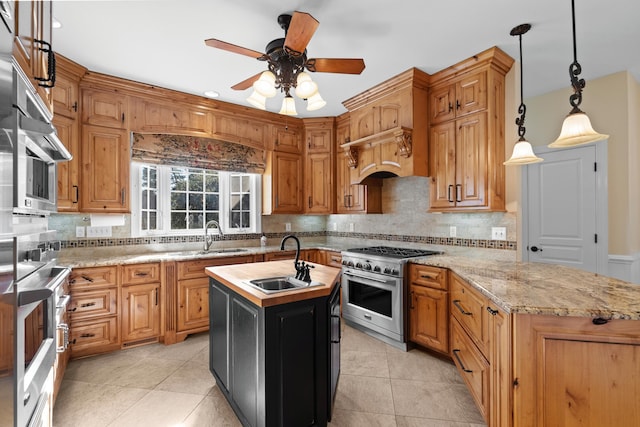 kitchen featuring sink, an island with sink, decorative light fixtures, and high end stainless steel range oven