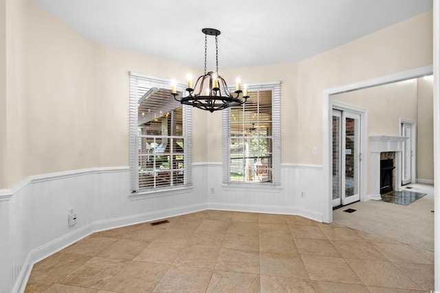 unfurnished dining area featuring light colored carpet, a notable chandelier, and a fireplace