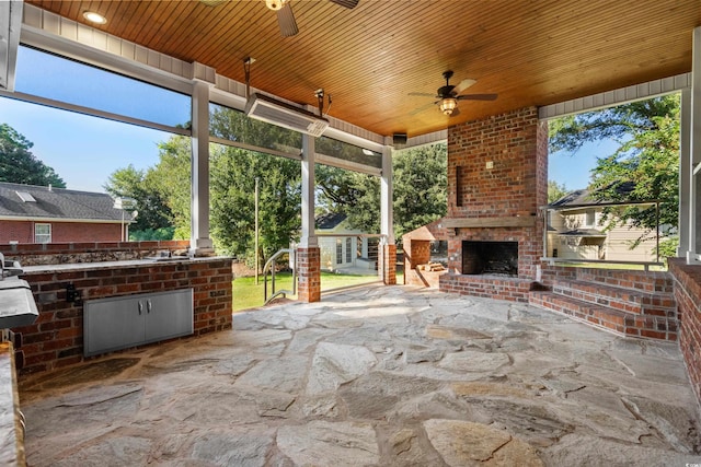 sunroom with an outdoor brick fireplace, wooden ceiling, and ceiling fan