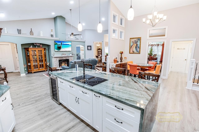 kitchen with pendant lighting, light hardwood / wood-style flooring, white cabinetry, a fireplace, and ceiling fan with notable chandelier