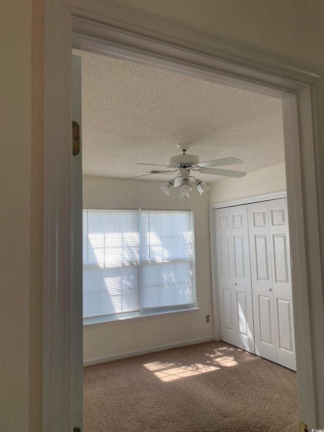 unfurnished bedroom with carpet, ceiling fan, a textured ceiling, and a closet