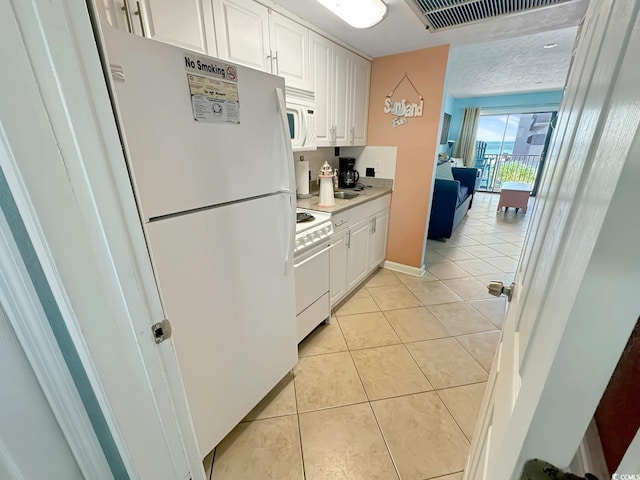 kitchen with white cabinets, light tile patterned flooring, and white appliances