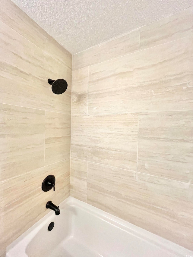 bathroom with a textured ceiling and tiled shower / bath