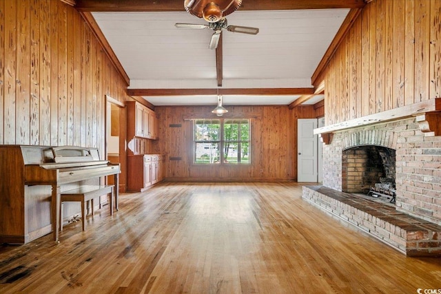 unfurnished living room featuring a fireplace, ceiling fan, wooden walls, wood-type flooring, and beamed ceiling