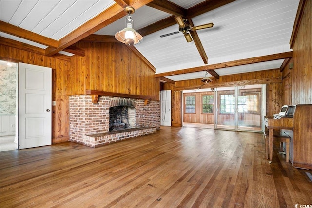 unfurnished living room featuring wood-type flooring, a brick fireplace, ceiling fan, and wooden walls