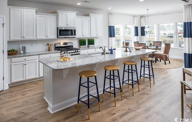 kitchen featuring white cabinets, light hardwood / wood-style floors, appliances with stainless steel finishes, and a kitchen island with sink