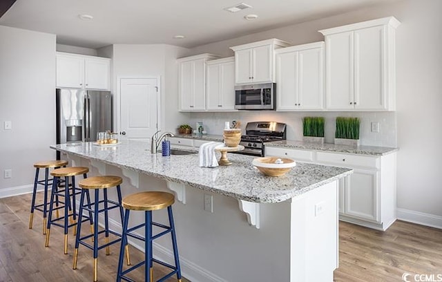 kitchen with white cabinets, appliances with stainless steel finishes, a kitchen island with sink, and sink