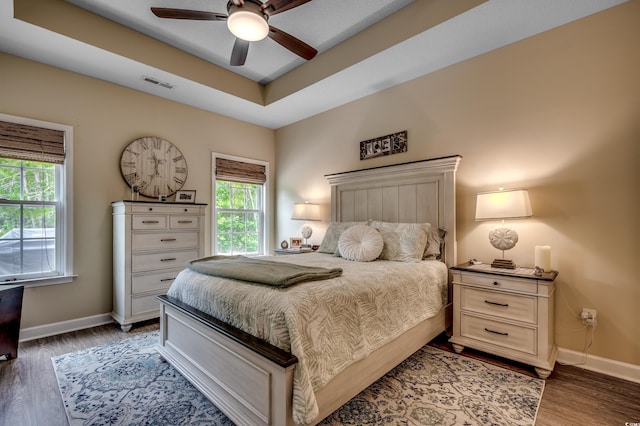 bedroom with a raised ceiling, dark hardwood / wood-style floors, and ceiling fan