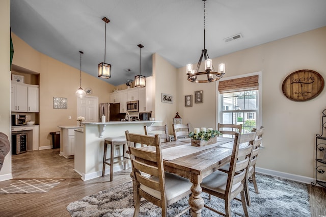 dining room with light hardwood / wood-style flooring, vaulted ceiling, a notable chandelier, and wine cooler