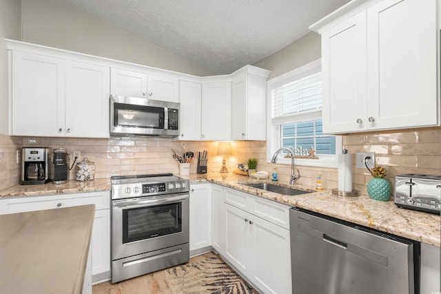 kitchen featuring white cabinets, appliances with stainless steel finishes, backsplash, and vaulted ceiling