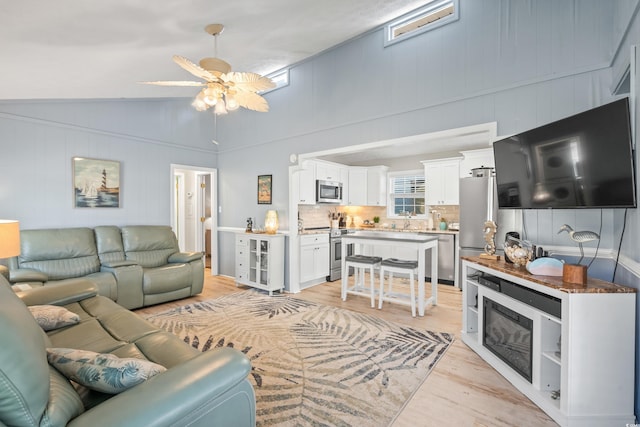 living room featuring ceiling fan, sink, vaulted ceiling, and light wood-type flooring