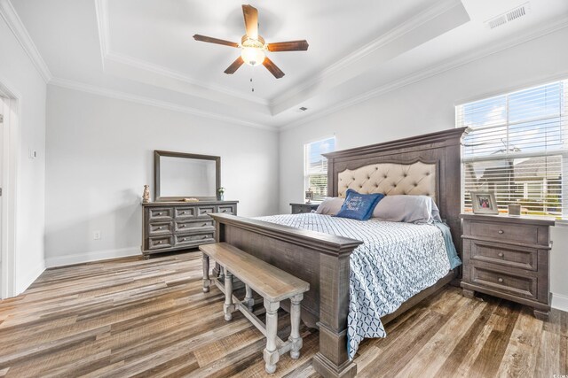 bedroom with hardwood / wood-style floors, ceiling fan, a tray ceiling, and multiple windows