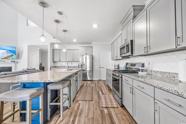 kitchen with appliances with stainless steel finishes, light wood-type flooring, a kitchen breakfast bar, backsplash, and gray cabinets