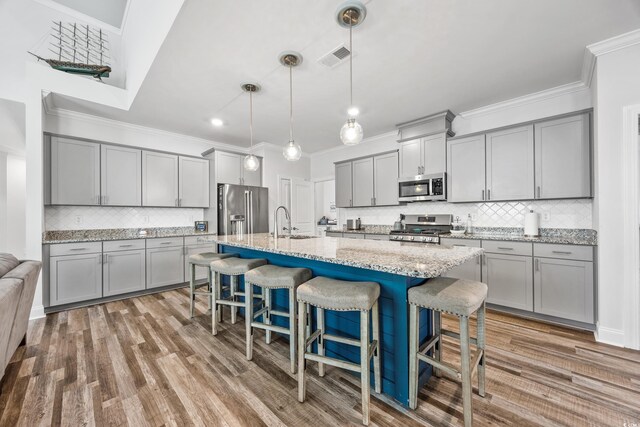 kitchen featuring a kitchen breakfast bar, hanging light fixtures, hardwood / wood-style flooring, an island with sink, and appliances with stainless steel finishes