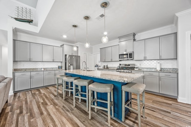 kitchen with a center island with sink, hanging light fixtures, a breakfast bar area, stainless steel appliances, and light stone countertops